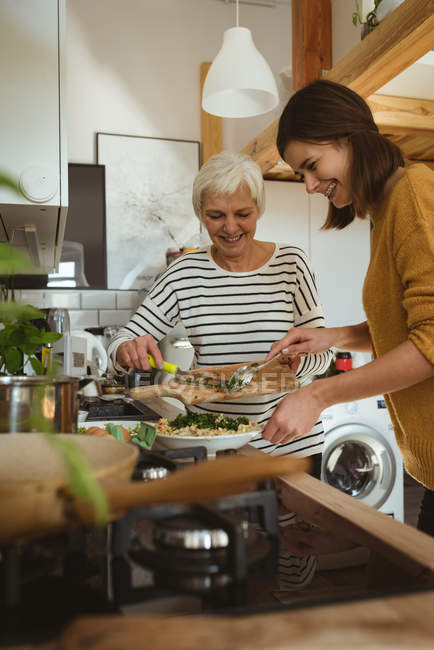 Mujer mayor sonriente e hija cocinando juntos en la cocina en casa - foto de stock