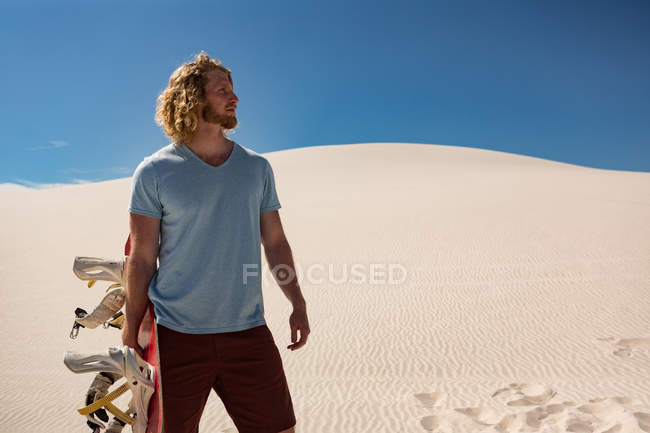 Человек с песчаной доской стоит в пустыне в солнечный день — стоковое фото