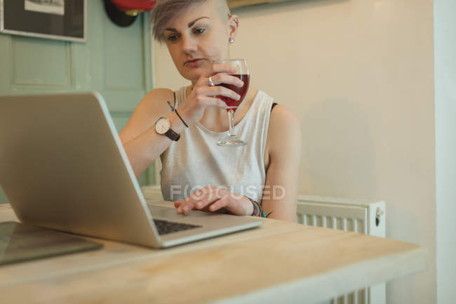 Donna che usa il computer portatile mentre beve vino a casa
. — Foto stock