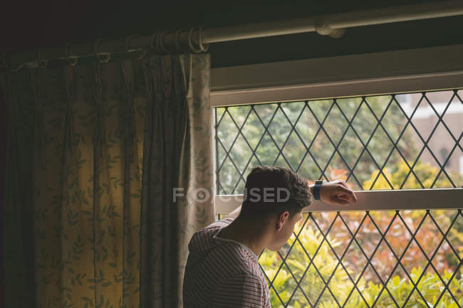 Uomo appoggiato e guardando attraverso la finestra a casa . — Foto stock