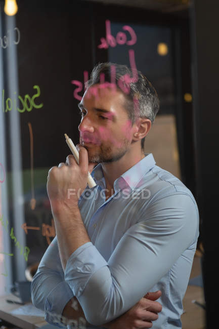 Thoughtful male executive reading notes on glass wall in office. — Stock Photo