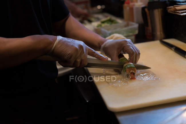 Koch schneidet Sushi-Rolle auf Schneidebrett — Stockfoto