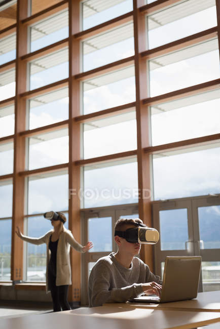 Студенти університету використовують ноутбук та гарнітуру віртуальної реальності за столом — стокове фото