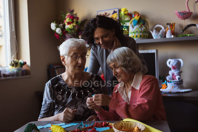 Deux femmes âgées faisant fleur artificielle avec gardien à la maison de soins infirmiers — Photo de stock