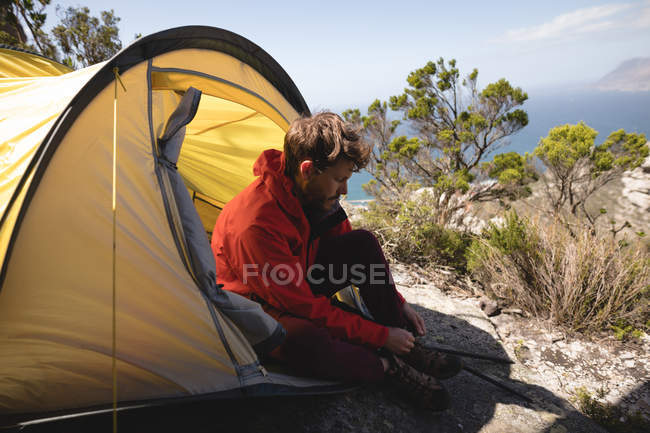 Hiker sitting in tent tying his shoelace on a sunny day — Stock Photo