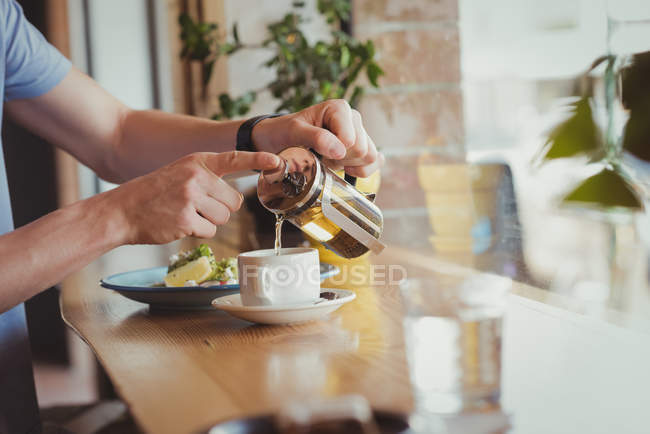 Средняя часть человека наливает кофе в чашку за столом — стоковое фото