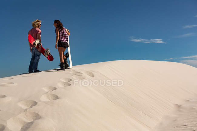 Casal com sandboard em pé na duna de areia no deserto — Fotografia de Stock