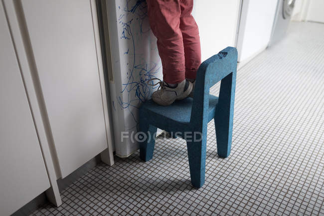 Boy standing on chair in kitchen at home, low section. — Stock Photo