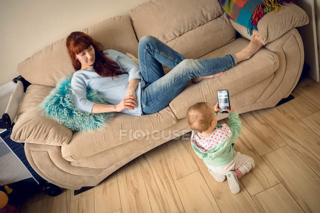 Малышка с матерью смотрит на мобильный телефон дома — стоковое фото