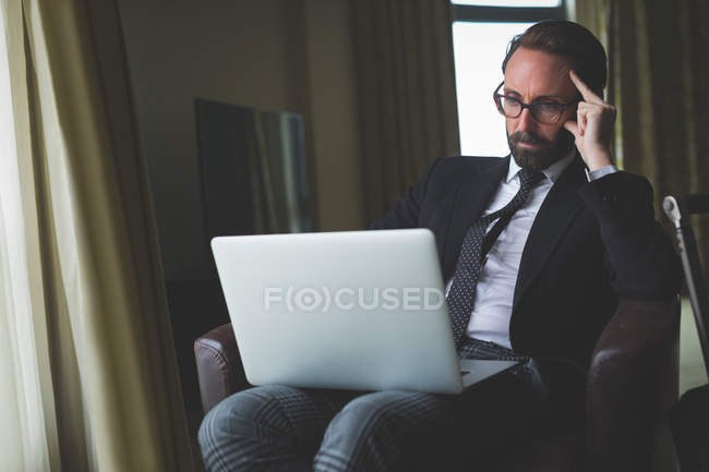 Homme d'affaires réfléchi utilisant un ordinateur portable dans la chambre d'hôtel — Photo de stock