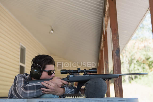 Uomo puntando fucile da cecchino al bersaglio nel poligono di tiro in una giornata di sole — Foto stock