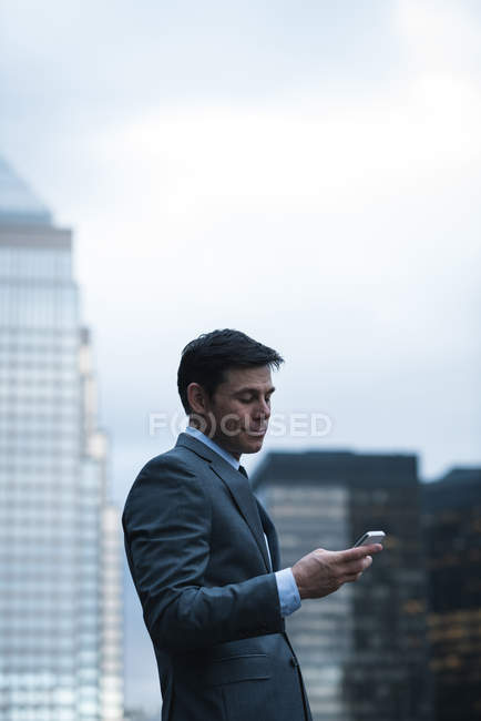 Вид сбоку на бизнесмена, использующего мобильный телефон на фоне небоскреба — стоковое фото