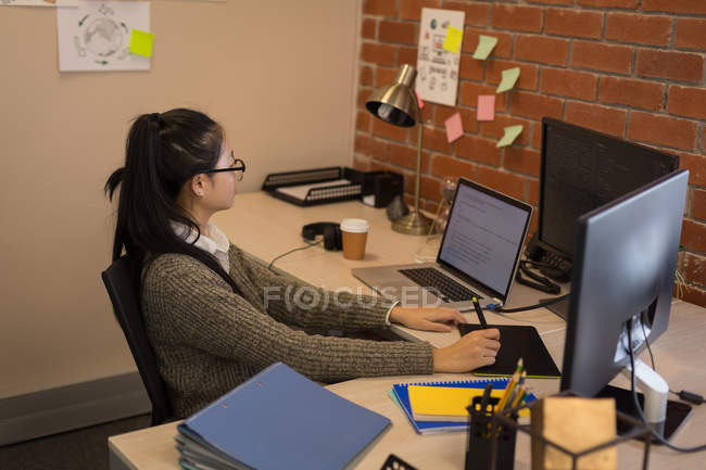 Diseñadora gráfica femenina usando tableta gráfica en el escritorio en la oficina - foto de stock