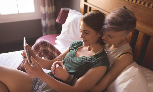 Lesbisches Paar umarmt und benutzt digitales Tablet im Schlafzimmer zu Hause. — Stockfoto