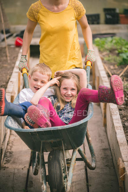 Mutter hat Spaß mit Kindern in Schubkarre im Gewächshaus — Stockfoto