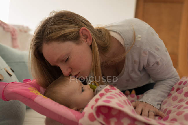 Mother kissing baby boy on bed at home. — Stock Photo