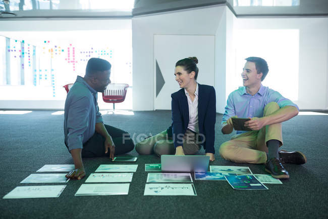 Male and female executives discussing over graphs and laptop in office — Stock Photo