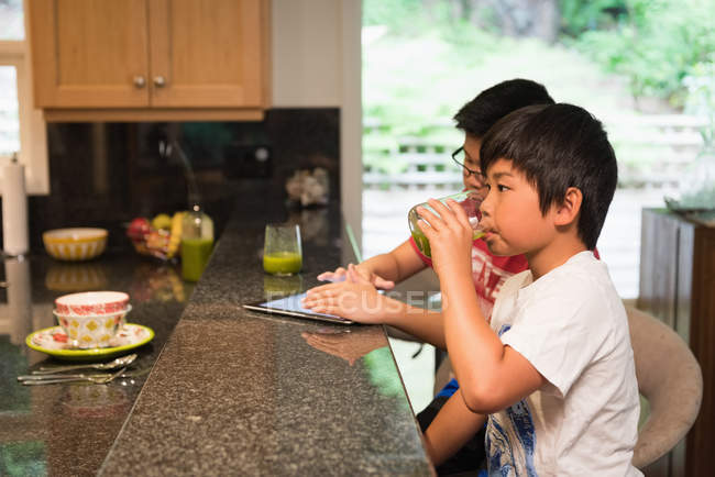 Siblings using digital tablet in kitchen at home — Stock Photo