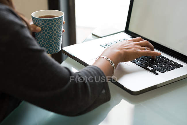 Ejecutivo femenino usando el ordenador portátil mientras toma una taza de café en la oficina - foto de stock