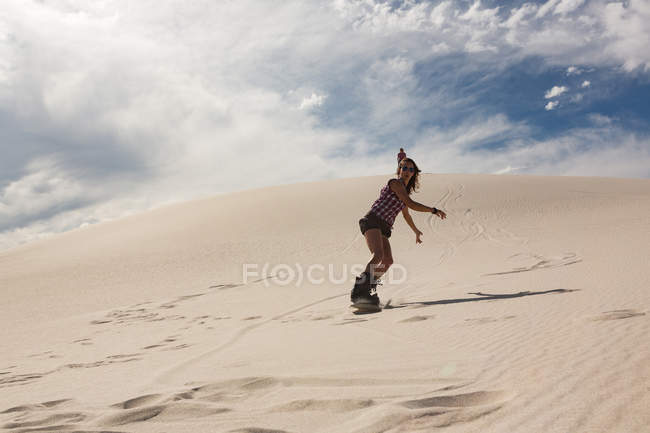 Sandboarding donna su dune di sabbia nel deserto — Foto stock