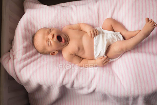 Newborn baby yawning on baby bed at home. — Stock Photo