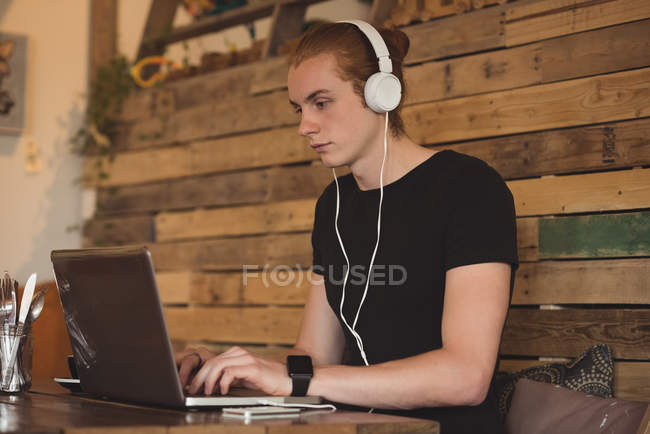 Man listening music on headphones while using laptop in cafe — Stock Photo
