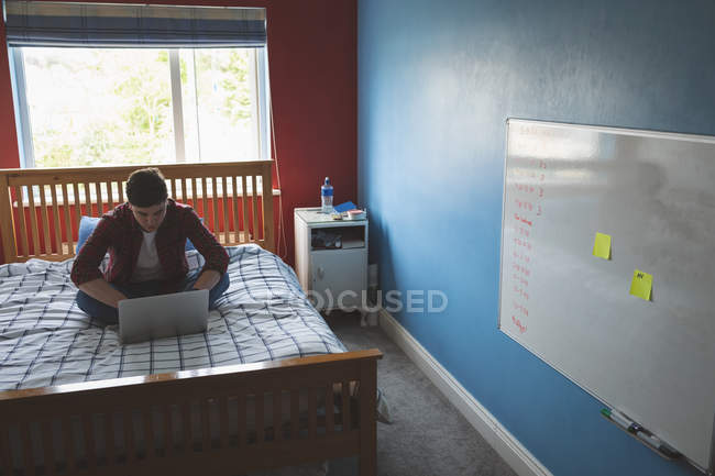 Hombre joven que trabaja con el ordenador portátil en la cama en casa . - foto de stock