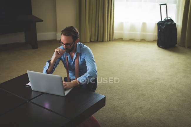 Empresario usando portátil en la mesa en la habitación del hotel - foto de stock