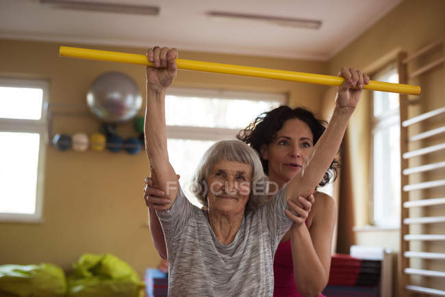 Terapeuta femenina que asiste a una mujer mayor con bastón de ejercicio en un hogar de ancianos - foto de stock