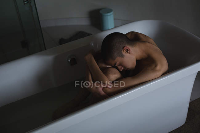 Depressed young man sitting in bathtub at bathroom — Stock Photo