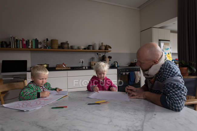 Pai ajudando as crianças no desenho à mesa na cozinha em casa . — Fotografia de Stock