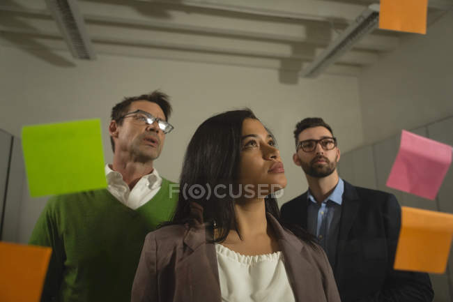 Business people discussing over sticky notes at office wall. — Stock Photo
