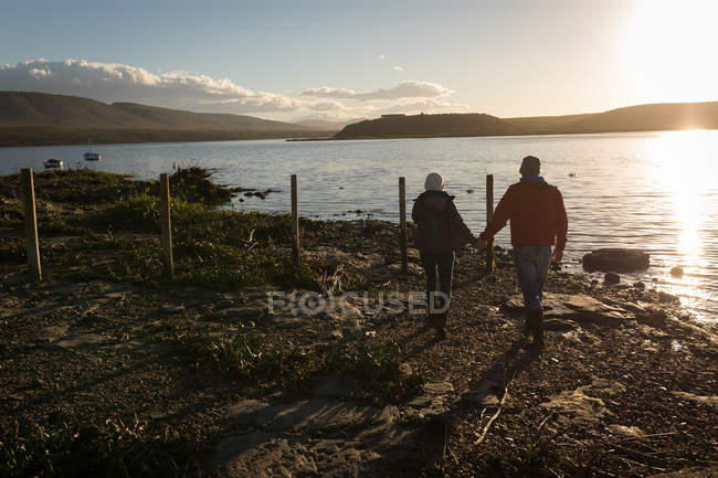 Romantic couple walking together while holding hands near river. — Stock Photo