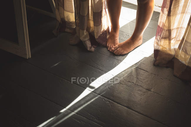 Gros plan des pieds féminins debout sur le plancher de bois près de la fenêtre à la maison . — Photo de stock
