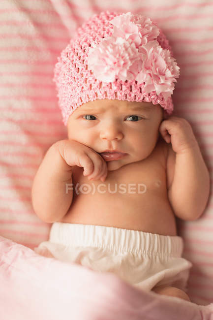 Neugeborenes Baby mit pinkfarbener Strickmütze entspannt auf dem heimischen Babybett. — Stockfoto