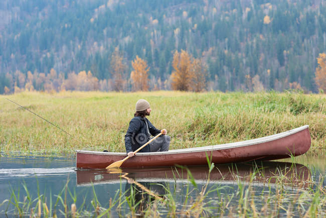 Man oaring canoa no rio perto de pastagens — Fotografia de Stock