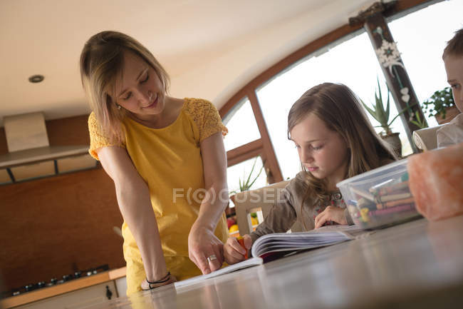 Mãe ajudando crianças com lição de casa na cozinha em casa — Fotografia de Stock