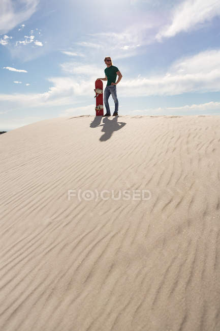 Hombre con sandboard de pie en el desierto en un día soleado - foto de stock