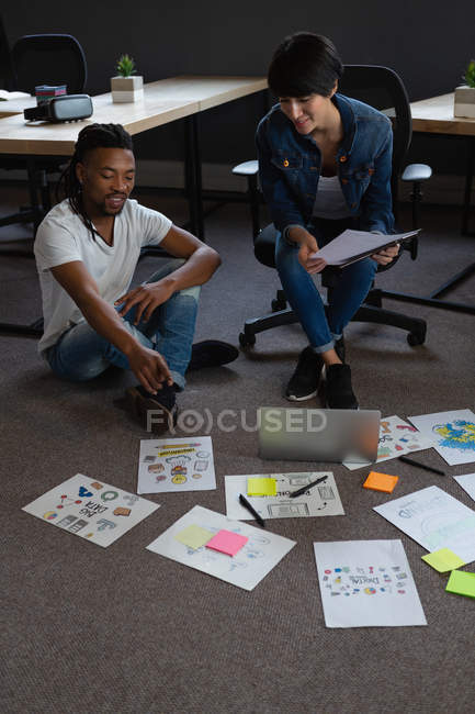 Compañeros de negocios discutiendo sobre documentos en el piso en la oficina . - foto de stock