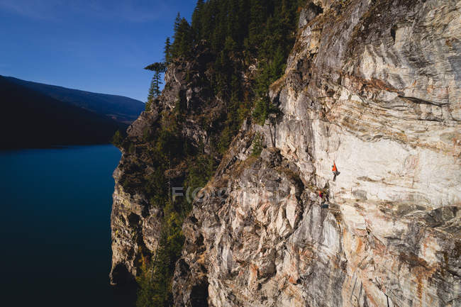 Entschlossener Bergsteiger, der die Klippe am Meer erklimmt — Stockfoto