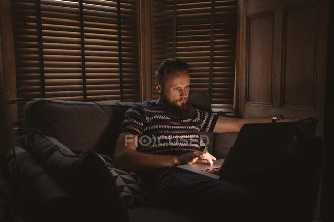 Mann im dunklen Zimmer sitzt auf Sofa und benutzt Laptop zu Hause — Stockfoto