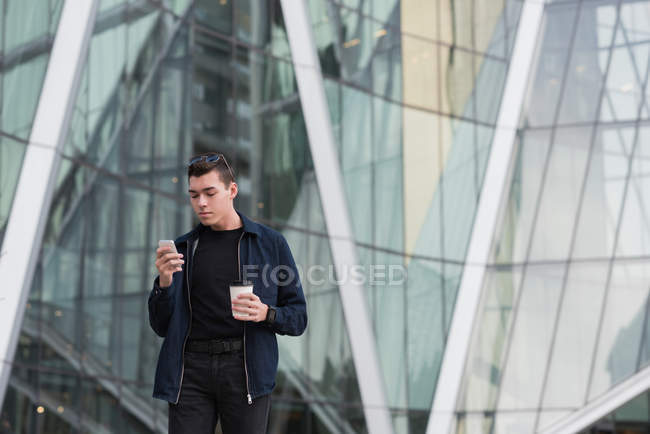 Homem usando telefone celular enquanto toma café em instalações de escritório — Fotografia de Stock