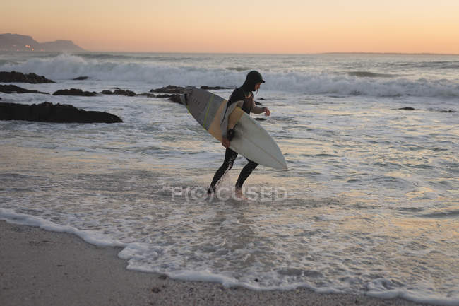 Серфер, що працює з дошкою для серфінгу в морі на заході сонця — стокове фото