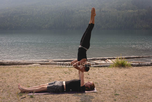 Pareja deportiva practicando acro yoga cerca de la costa del mar en un día soleado - foto de stock