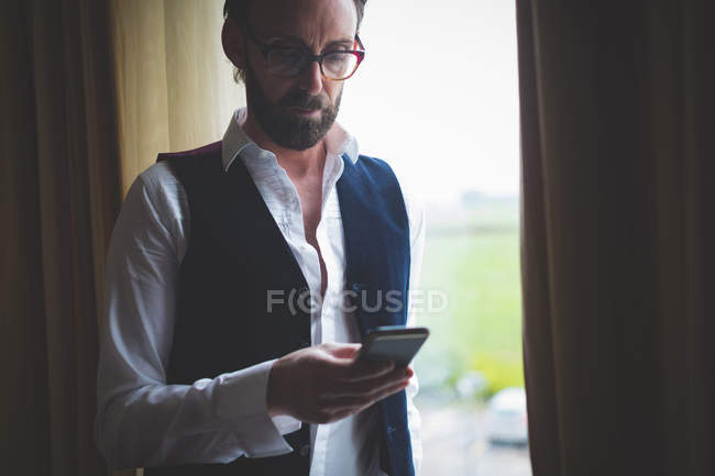 Бізнесмен, використовуючи мобільний телефон біля вікна в готельному номері — стокове фото