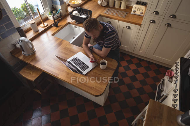 Чоловік сидить на стільці використовуючи свій мобільний телефон на кухні вдома — стокове фото
