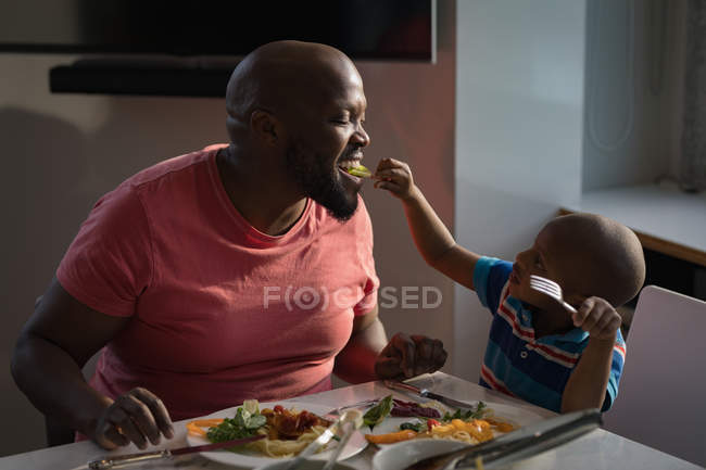 Son feeding father vegetables at dinning table at home. — Stock Photo