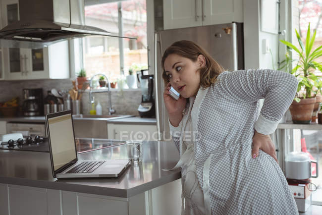 Pregnant woman talking on mobile phone while using laptop — Stock Photo
