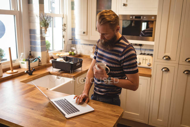 Мужчина пьет кофе, пользуясь ноутбуком дома — стоковое фото