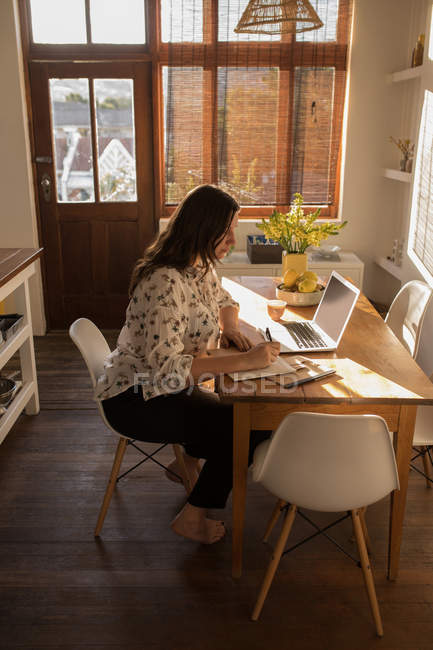 Femme caucasienne utilisant un ordinateur portable à la table à la maison — Photo de stock